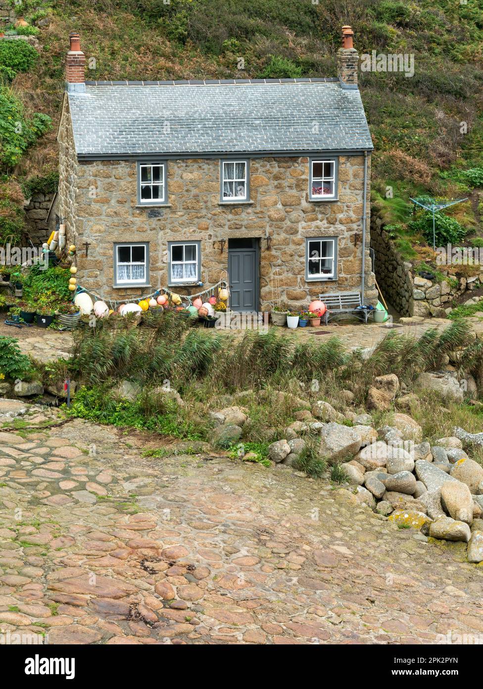 Bella vecchia pietra di granito Cornish cottage sul mare con tetto in ardesia e galleggianti da pesca e boe a Penberth Cove, Cornwall, Regno Unito Foto Stock