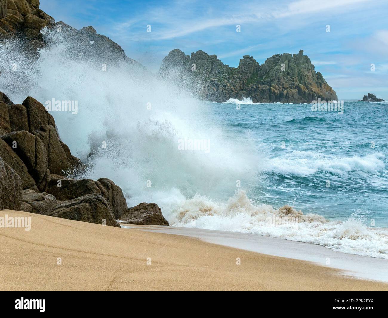 Mare, surf, onde e spray con Logan Rock promontorio in lontananza, Porthcurno spiaggia, Cornovaglia, Inghilterra, Regno Unito Foto Stock