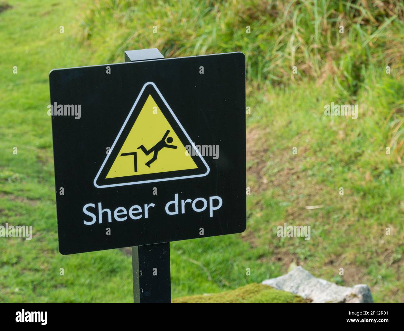 Cartello di pericolo "Sheer Drop" con simbolo di caduta uomo in triangolo giallo con testo in lingua inglese riportato di seguito Foto Stock