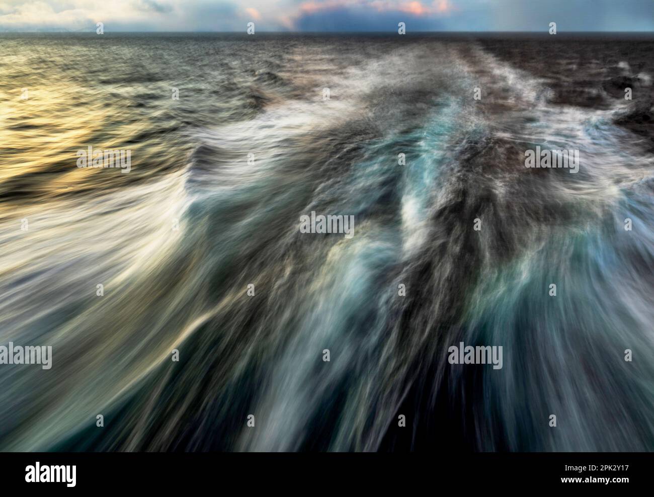 Potenza dell'onda in esposizione prolungata, acqua sfocata, illuminazione della superficie del mare al tramonto. Foto Stock