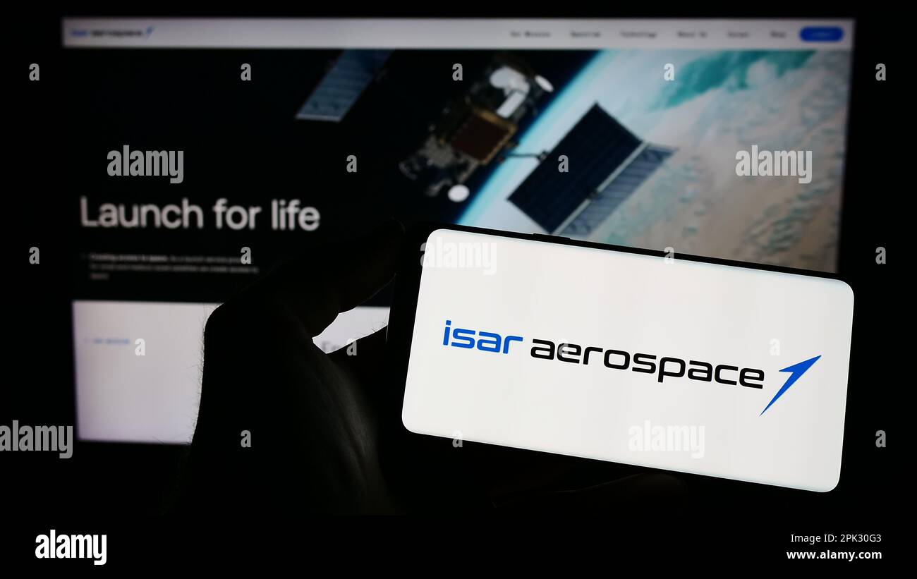 Persona che tiene un telefono cellulare con il logo della società Isar Aerospace Technologies GmbH sullo schermo di fronte alla pagina web aziendale. Messa a fuoco sul display del telefono. Foto Stock