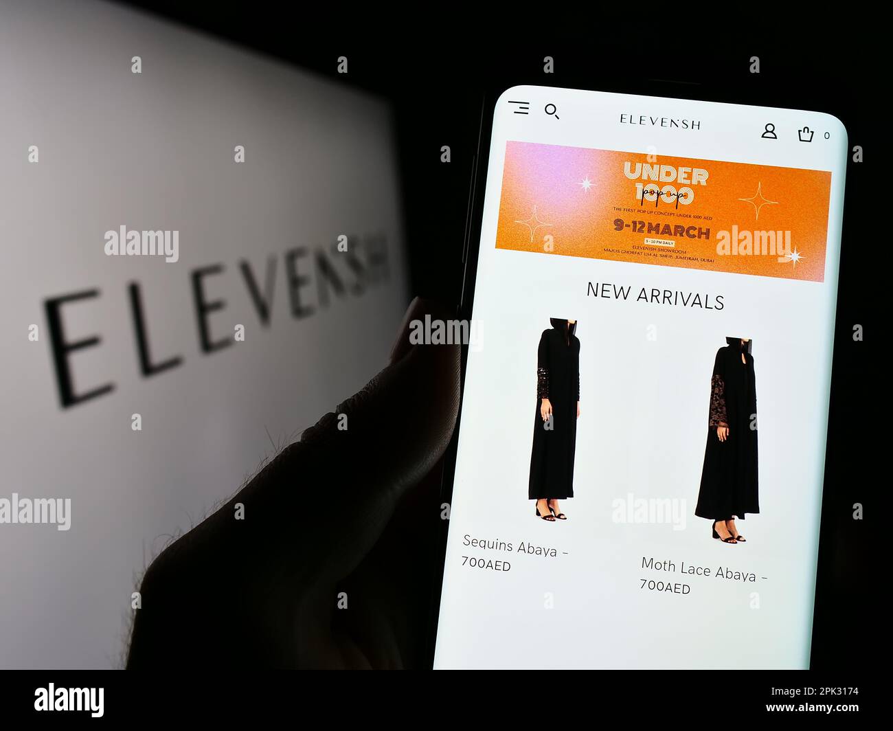 Persona che tiene il cellulare con la pagina web della società di commercio elettronico ELEVENiSH Emirati sullo schermo di fronte al logo. Messa a fuoco al centro del display del telefono. Foto Stock