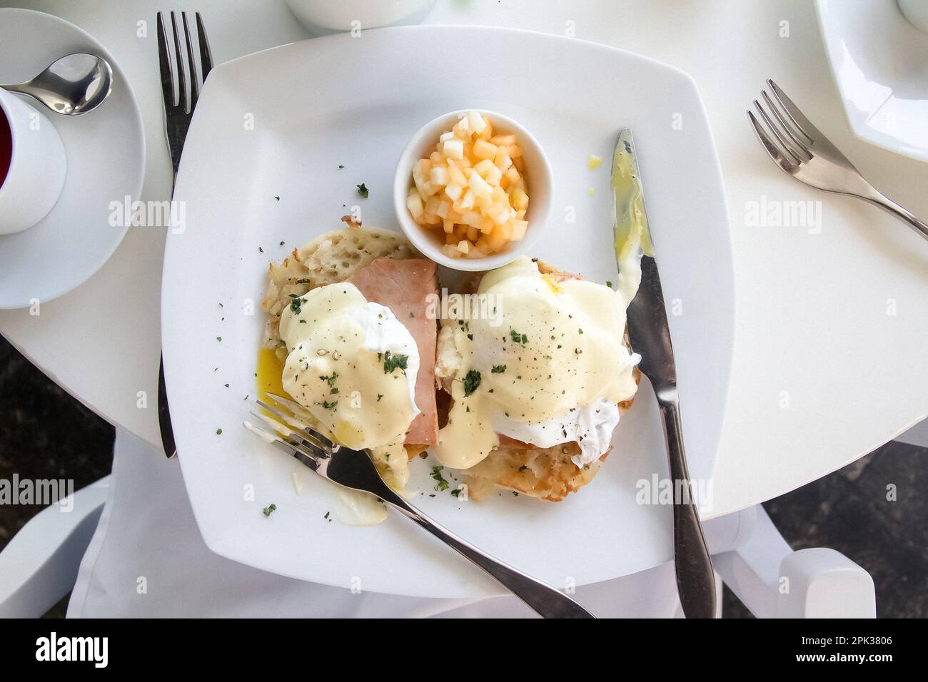 Colazione con uova alla benedict su un piatto bianco e tavolo con argenteria Foto Stock