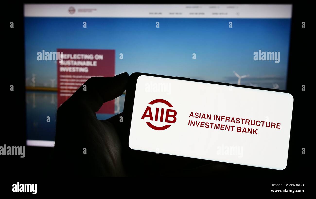 Persona che tiene il cellulare con il logo della Banca asiatica d'investimento per le infrastrutture (AIIB) sullo schermo di fronte alla pagina web. Messa a fuoco sul display del telefono. Foto Stock