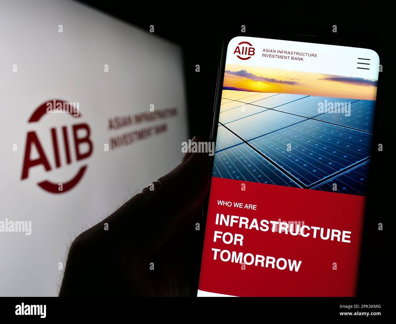 Persona che tiene il cellulare con il logo della Banca asiatica d'investimento per le infrastrutture (AIIB) sullo schermo di fronte al sito web aziendale. Messa a fuoco sul display del telefono. Foto Stock