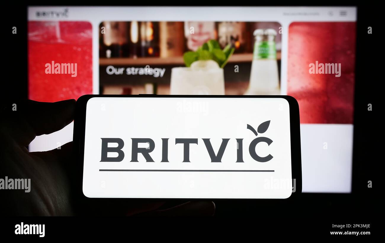 Persona in possesso di smartphone con il logo della società britannica di bevande analcoliche Britvic plc sullo schermo di fronte al sito Web. Messa a fuoco sul display del telefono. Foto Stock