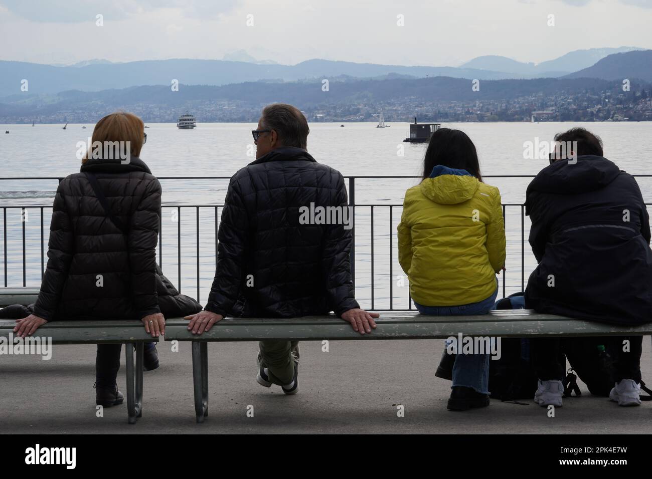 Due coppie eterosessuali seduti su una panchina sulla riva del lago di Zurigo. Vista posteriore con il lago e le Alpi svizzere sullo sfondo. Foto Stock