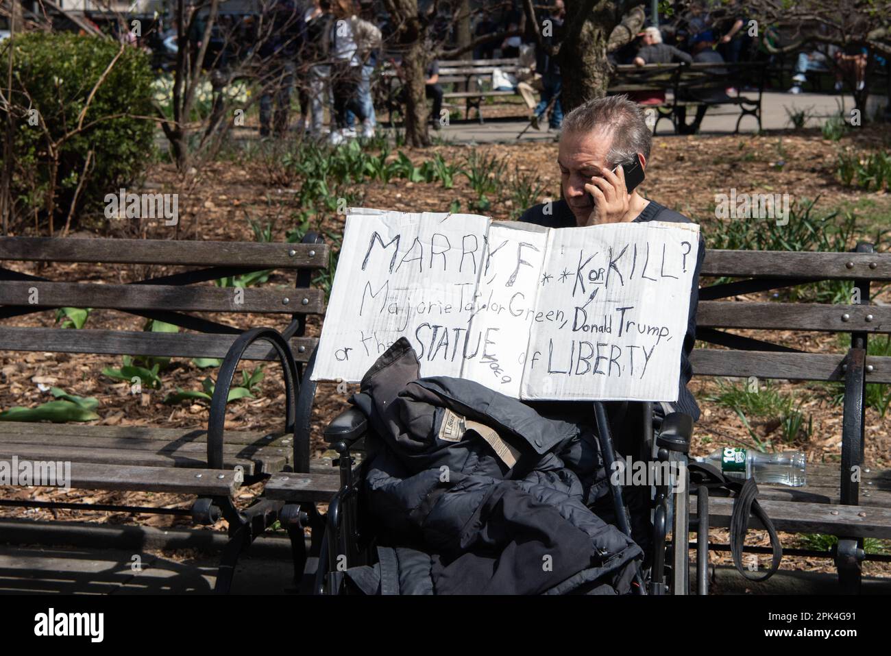 Un uomo si siede su una panchina al di fuori dell'arraignment dell'ex presidente Donald Trump tenendo un segno chiedendo 'sposare, F**k o uccidere? Marjorie Taylor Green, Donald Trump o la Statua della libertà" Foto Stock