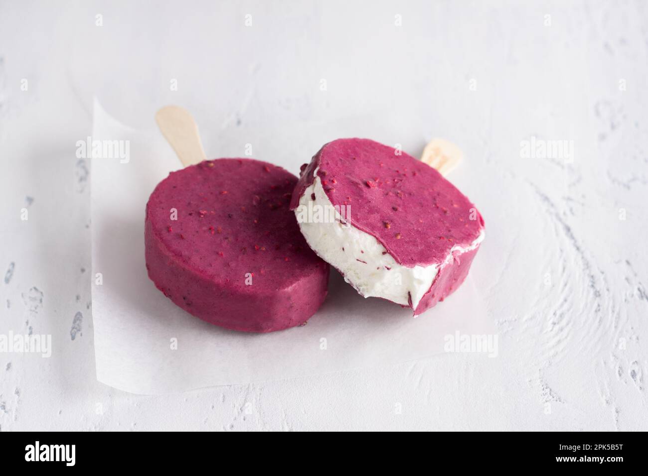 Gelato alla vaniglia, papicola su bastone, glassa di melograno con pezzi di melograno su fondo grigio chiaro Foto Stock