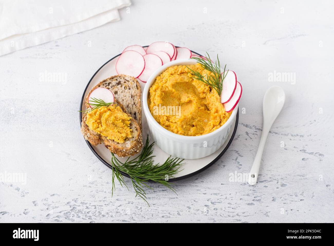 Fate una semplice frittura di uova o immergetevi con carote e cipolle fritte in un recipiente bianco decorato con fette di ravanello e aneto con pane di cereali su un dorso grigio chiaro Foto Stock