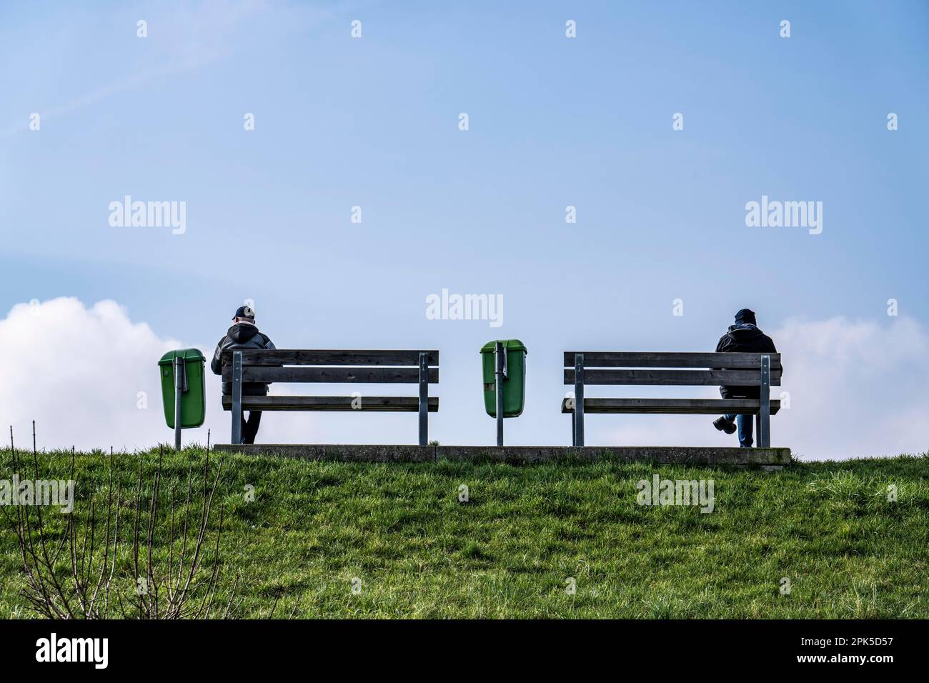 Panchine su una diga sul Weser a Bremerhaven, due persone sedute simmetricamente lontano l'una dall'altra sulle panchine Brema, Germania Foto Stock