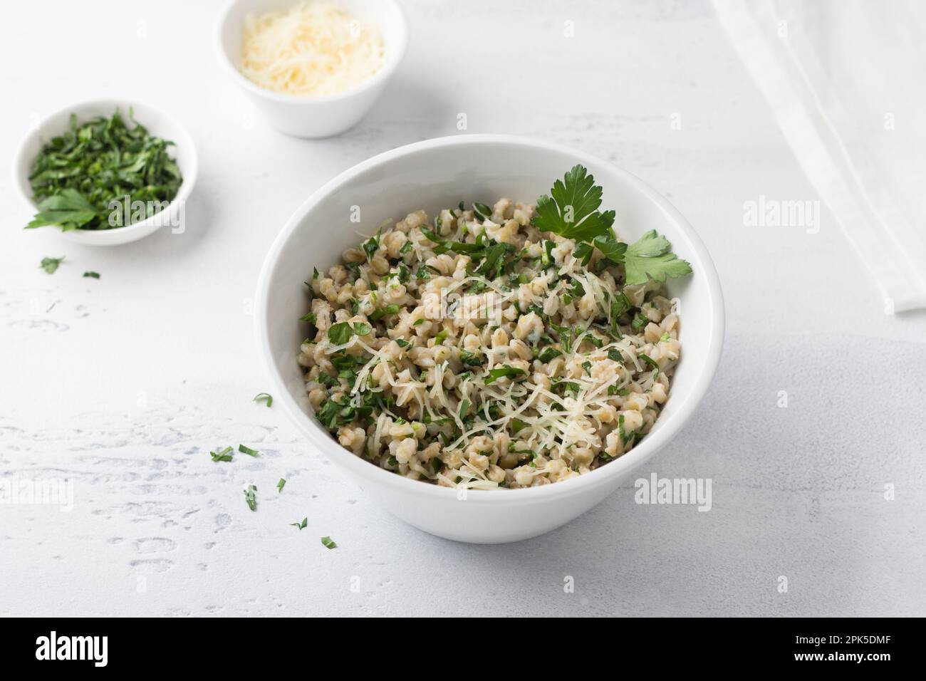 Orzo perlato con formaggio ed erbe in ciotola di ceramica bianca su sfondo grigio chiaro, vista dall'alto. Colazione deliziosa e sana Foto Stock