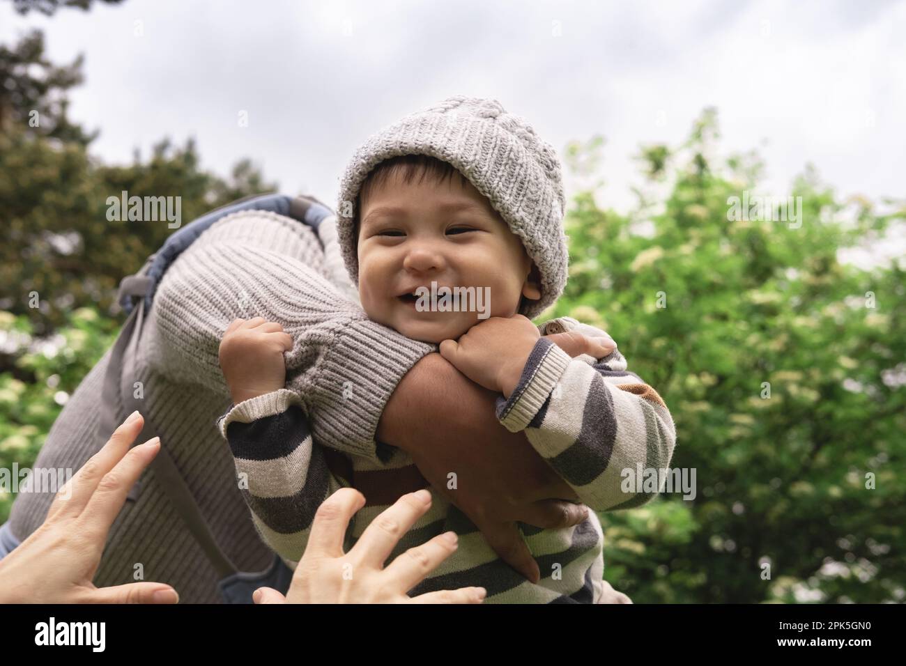 Primo piano del nuovo papà che gioca con il bambino, sollevando, gettando il bambino cute in su nell'aria nella natura. Ragazzo sorridente che tiene con forza le braccia del padre, le mani della madre. M Foto Stock
