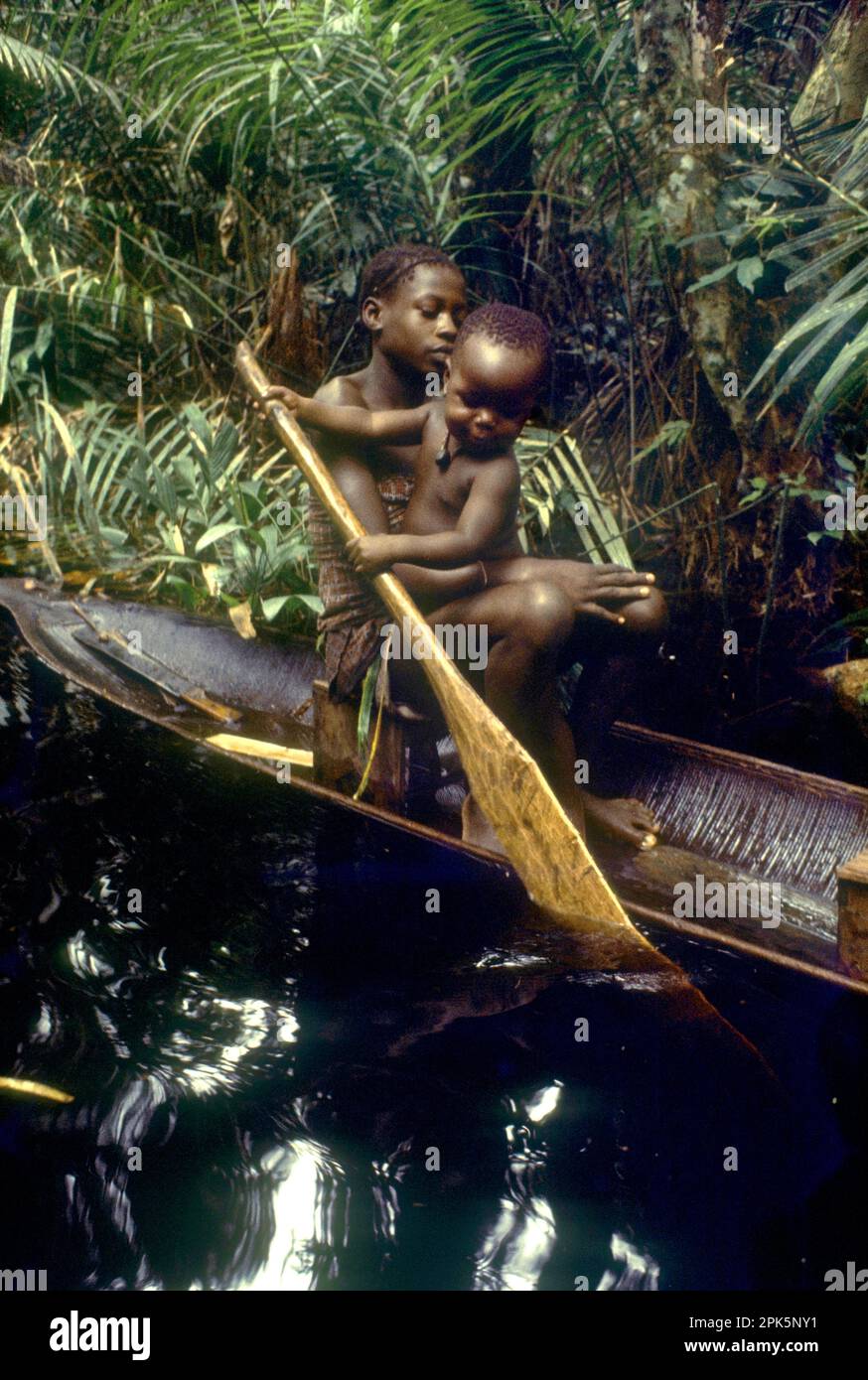 Ragazza del gruppo etnico Libinza con bambino che impara a pagaiare in canoa nella foresta paludosa. Zona fluviale di Ngiri, Repubblica Democratica del Congo, Africa centrale. Foto Stock