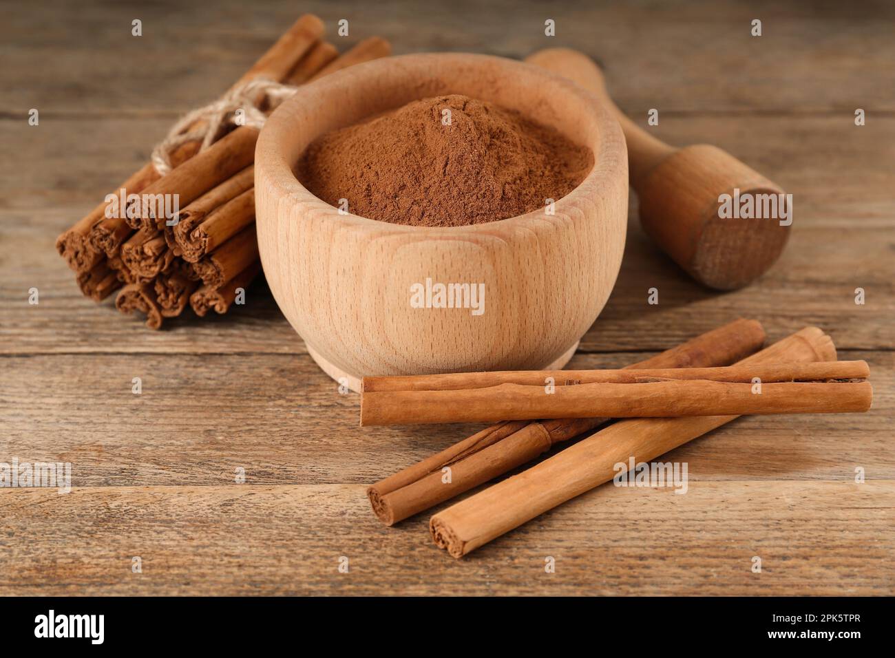 Cannella in polvere aromatica in mortaio, bastoncini e pestello su tavola di legno Foto Stock