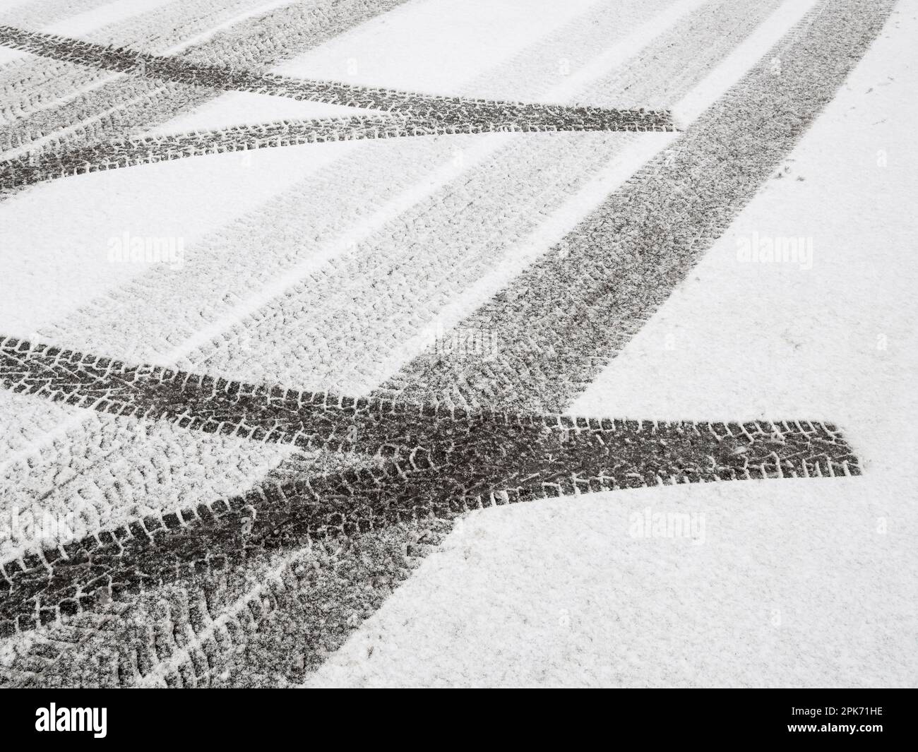Neve fresca e intatta copre la strada invernale. I contrassegni degli pneumatici creano un motivo di linee vaganti attraverso il fresco parcheggio bianco. Foto Stock