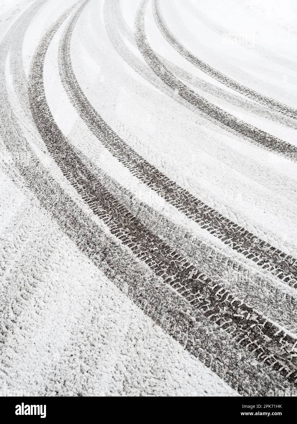 Neve fresca e intatta copre la strada invernale. I contrassegni degli pneumatici creano un motivo di linee vaganti attraverso il fresco parcheggio bianco. Foto Stock