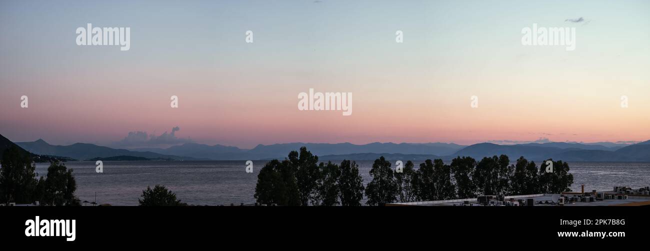 Panorama dell'alba dall'isola di Corfù con vista sulle montagne della penisola balcanica di Grecia, Moraitika, Corfù. A Foreground ci sono edifici di hotel, alberi Foto Stock