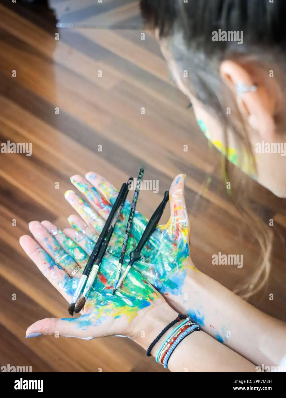 Pittore femminile con pennelli e mani piene di vernice colorata. Ragazza pittura a casa, interior design, opere d'arte, attività a casa Foto Stock