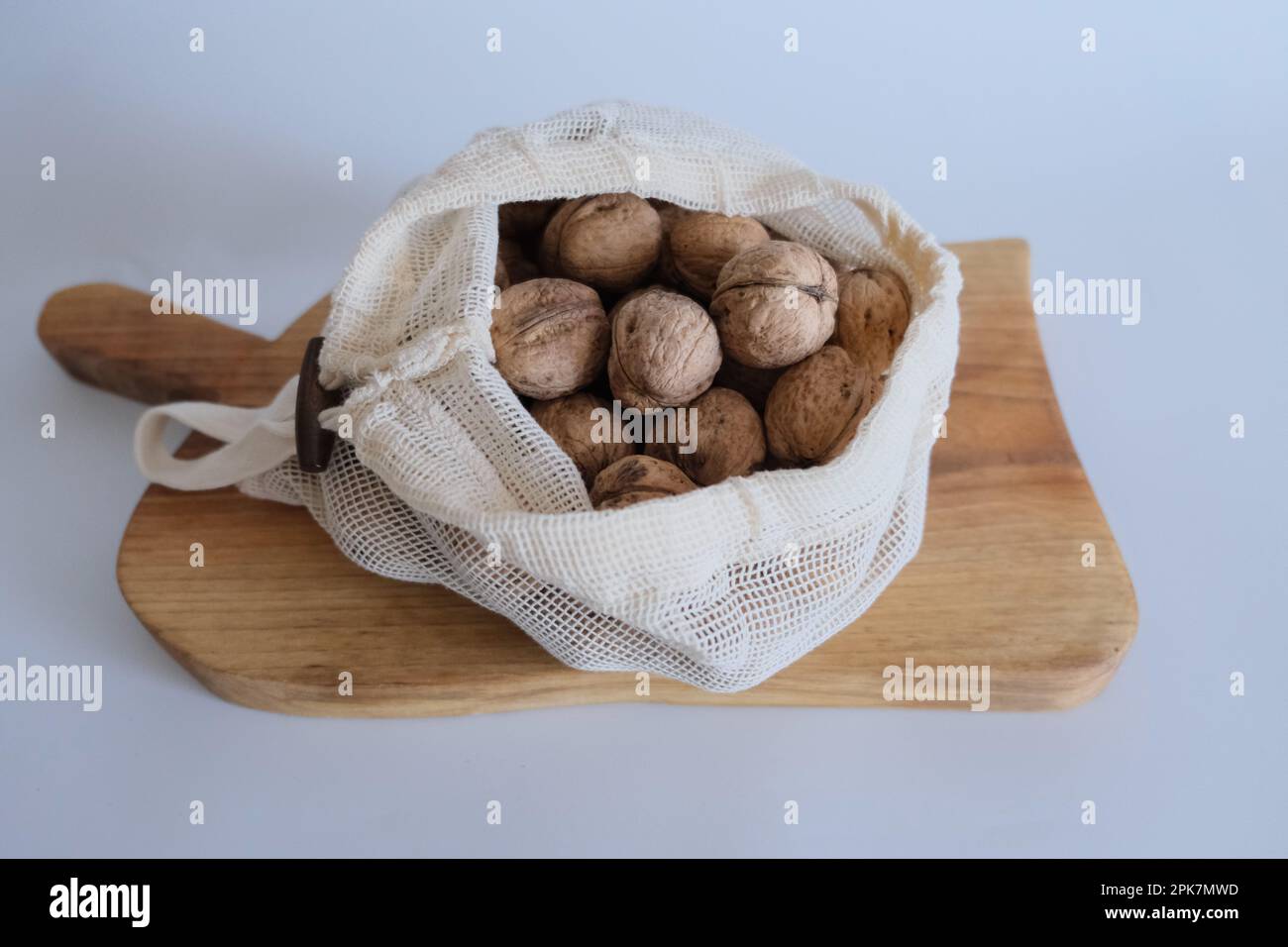 Noci sgusciate, mucchio di noci con sgusciate in sacchi di stoffa bianca su fondo bianco con tagliere di legno. Foto Stock