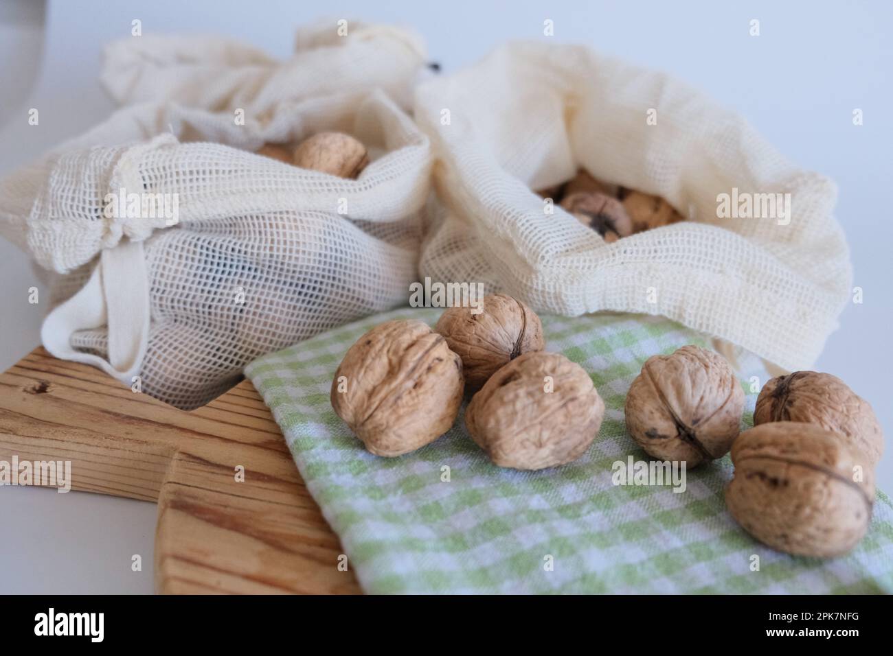Noci sgusciate, mucchio di noci sgusciate in sacchetti di stoffa bianca con tagliere in legno e panno da cucina a scacchi verde e bianco. Foto Stock
