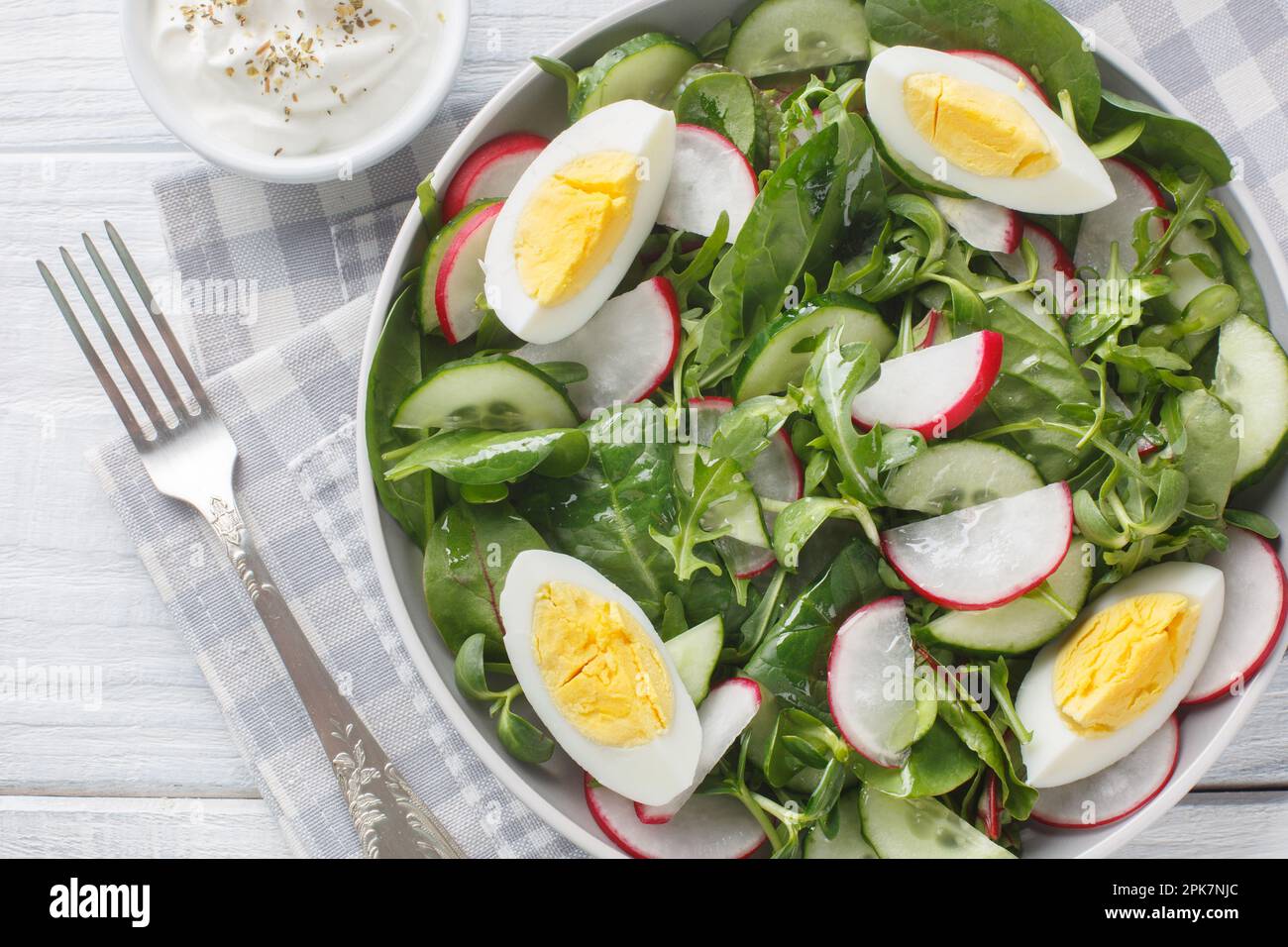 Insalata di verdure primaverili con ravanello, cetriolo, lattuga mix, spinaci e uova primo piano in un piatto su un tavolo di legno primo piano sul piatto sul tavolo. H Foto Stock