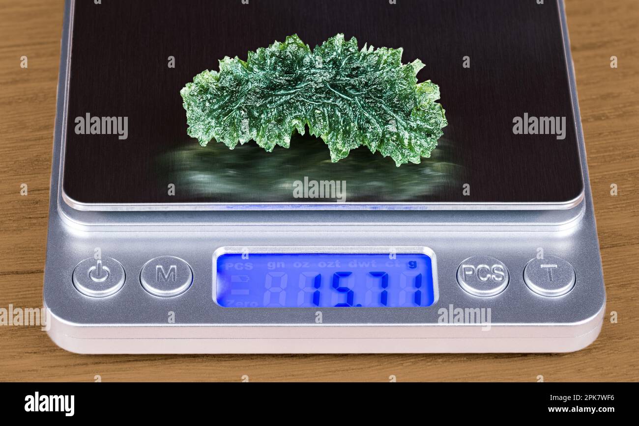 Primo piano di una bella gemma verde di moldavite su bilancia con display digitale. Determinazione accurata del peso della gemma grezza dal vetro meteoritico. Foto Stock