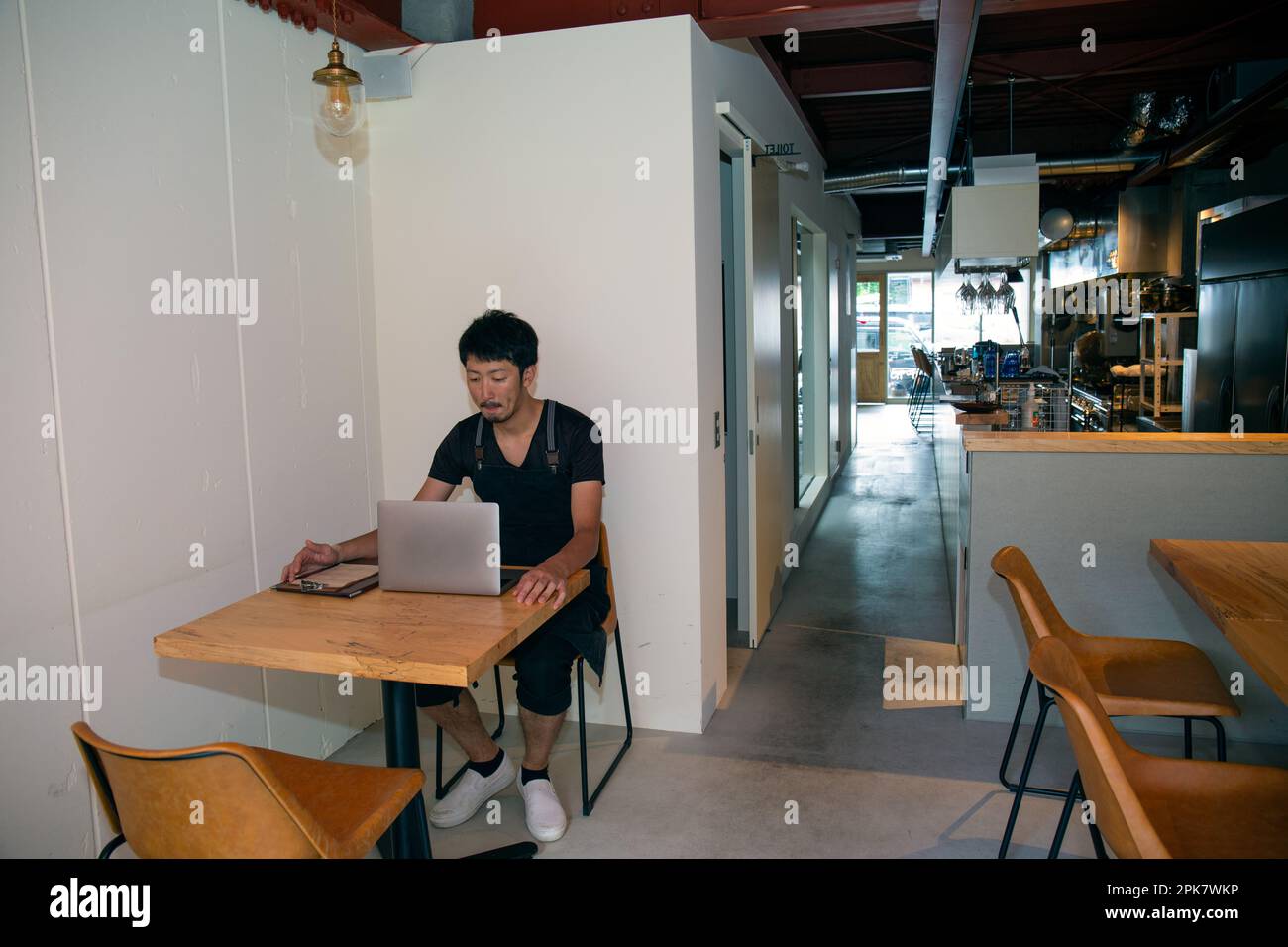 Un uomo seduto a un tavolo con un computer portatile, proprietario e gestore di un piccolo ristorante. Foto Stock