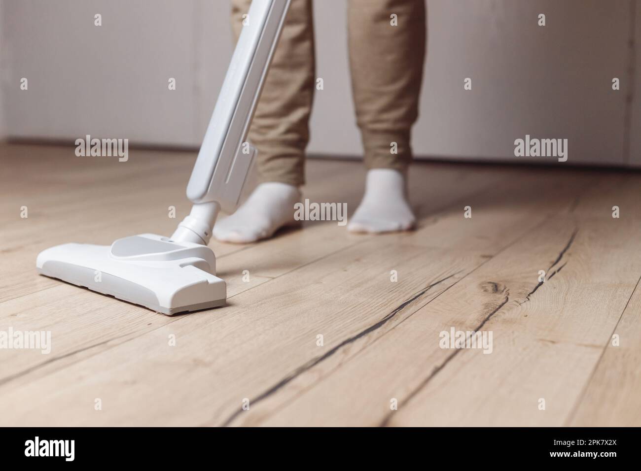 Donna pulizia pavimento in legno con aspirapolvere senza fili. Vista ravvicinata della spazzola e delle gambe dell'aspirapolvere in calzini bianchi sullo sfondo Foto Stock