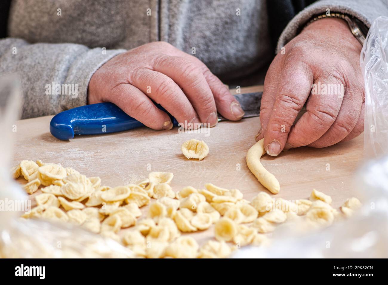 Mani rugose di una donna anziana che prepara orecchiette o orecchiette fresche, a base di grano duro e acqua, pasta fatta a mano tipica pugliese Foto Stock