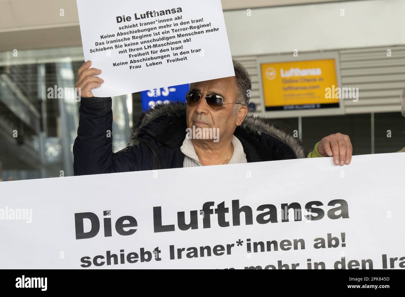 Francoforte, Germania. 06 aprile 2023. Un dimostratore tiene un cartello di fronte ai banchi Lufthansa durante una manifestazione all'aeroporto di Francoforte contro il coinvolgimento della compagnia aerea nei voli di deportazione per l'Iran, che recita: "Lufthansa sta deportando gli iraniani! Più recentemente, ci sono stati due voli con persone deportate in Iran. Foto: Sebastian Gollnow/dpa/Alamy Live News Foto Stock