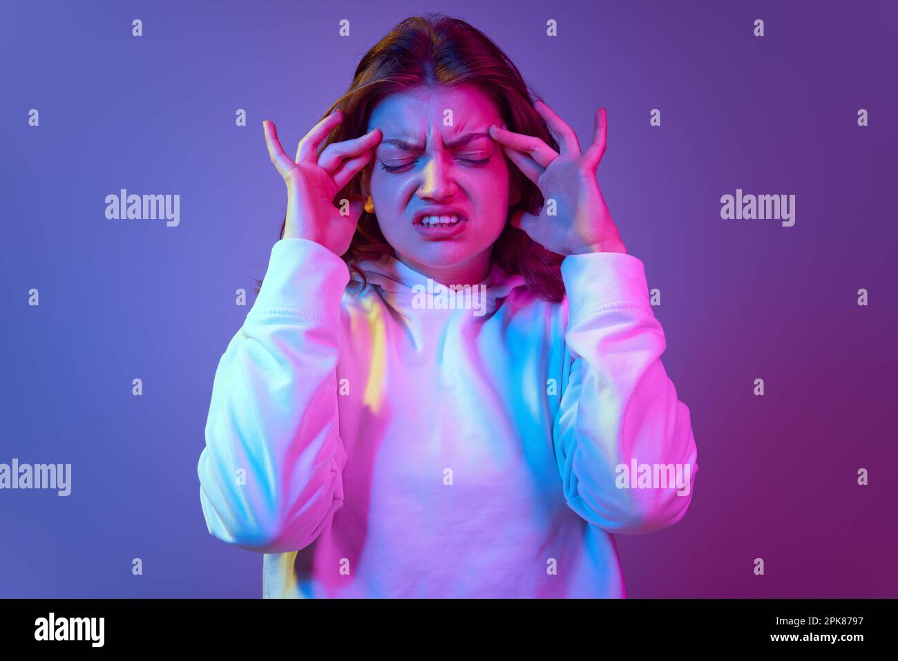 Giovane ragazza che tocca la testa in emicrania contro sfondo blu sfumato viola studio in luce al neon. Scadenze, brainstorming Foto Stock