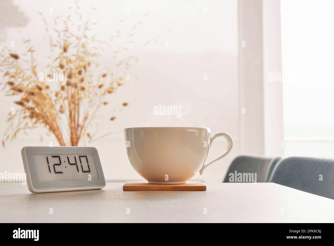Concetto di tempo di pausa caffè. Una tazza di caffè caldo e un orologio digitale sul tavolo. Interni accoglienti sfondo a tema Foto Stock
