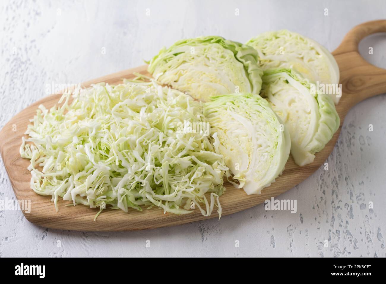 Cavolo bianco giovane, tagliato a strisce e tagliato a segmenti su un asse di legno, sfondo azzurro, vista dall'alto. Cucinare una deliziosa insalata sana o Foto Stock