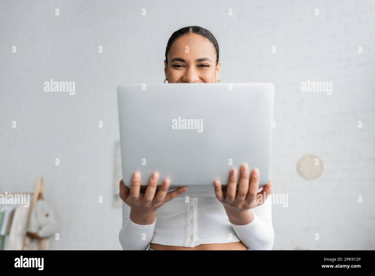 felice studente afro-americano che copre metà del volto mentre tiene il portatile, immagine di borsa Foto Stock