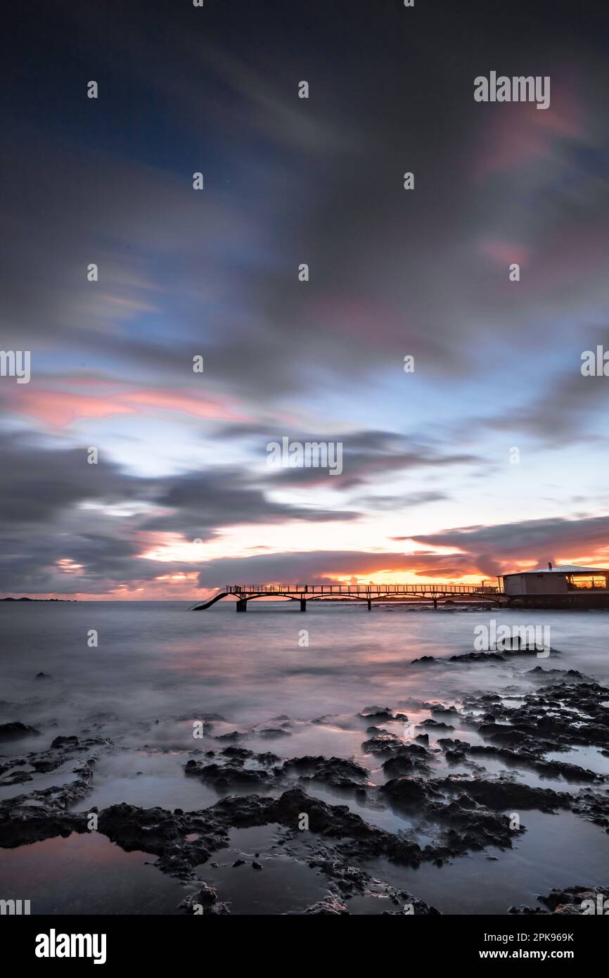 Alba sulla spiaggia, rocce laviche e spiaggia sabbiosa in lunga esposizione. Posto romantico con molo al mattino. Playa de la Barreta, Parco Nazionale di Corralejo, Isole Canarie, Spagna Foto Stock