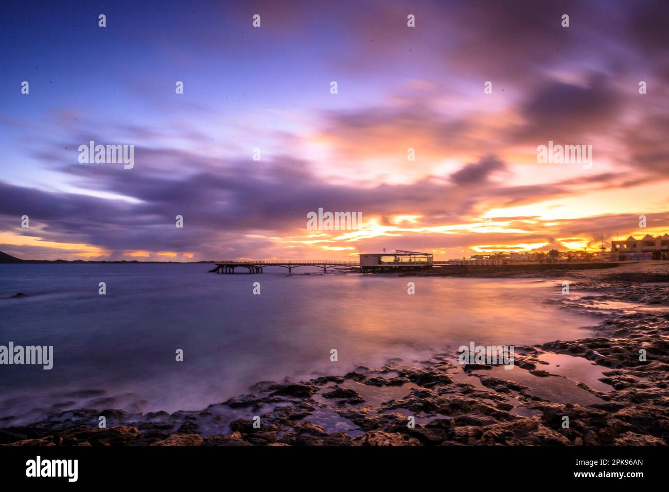 Alba sulla spiaggia, rocce laviche e spiaggia sabbiosa in lunga esposizione. Posto romantico con molo al mattino. Playa de la Barreta, Parco Nazionale di Corralejo, Isole Canarie, Spagna Foto Stock