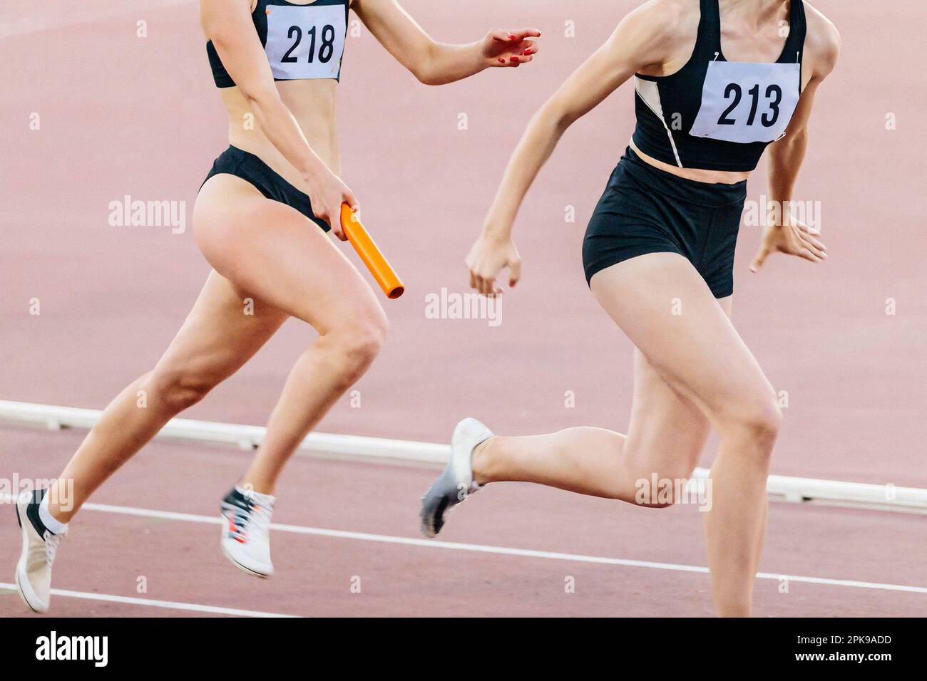 le donne che corrono in staffetta corrono nel campionato di atletica estiva, passando il testimone due atlete Foto Stock
