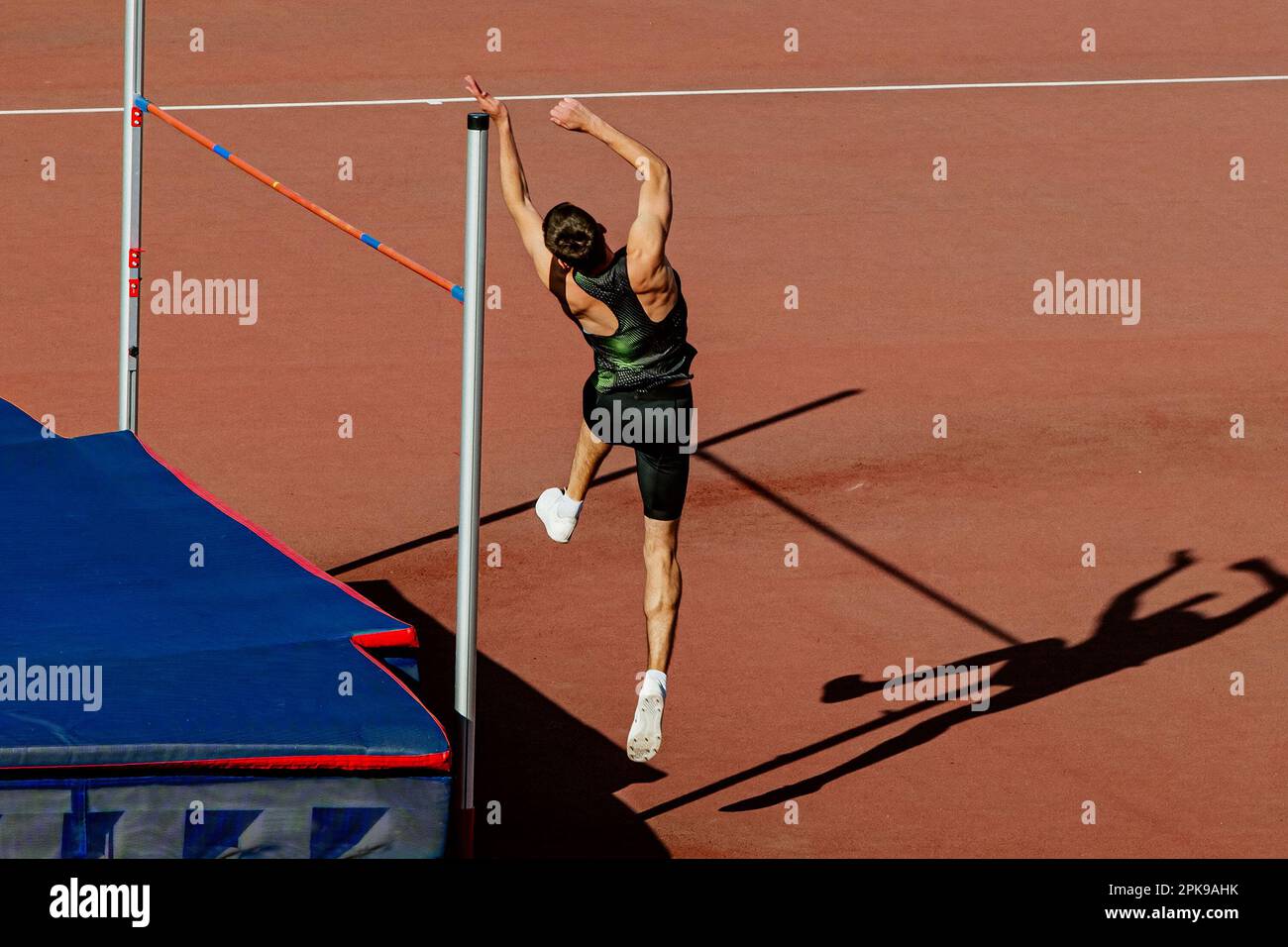 atleta maschile salto alto nei campionati estivi di atletica, jumper ombra su pista rossa stadio Foto Stock