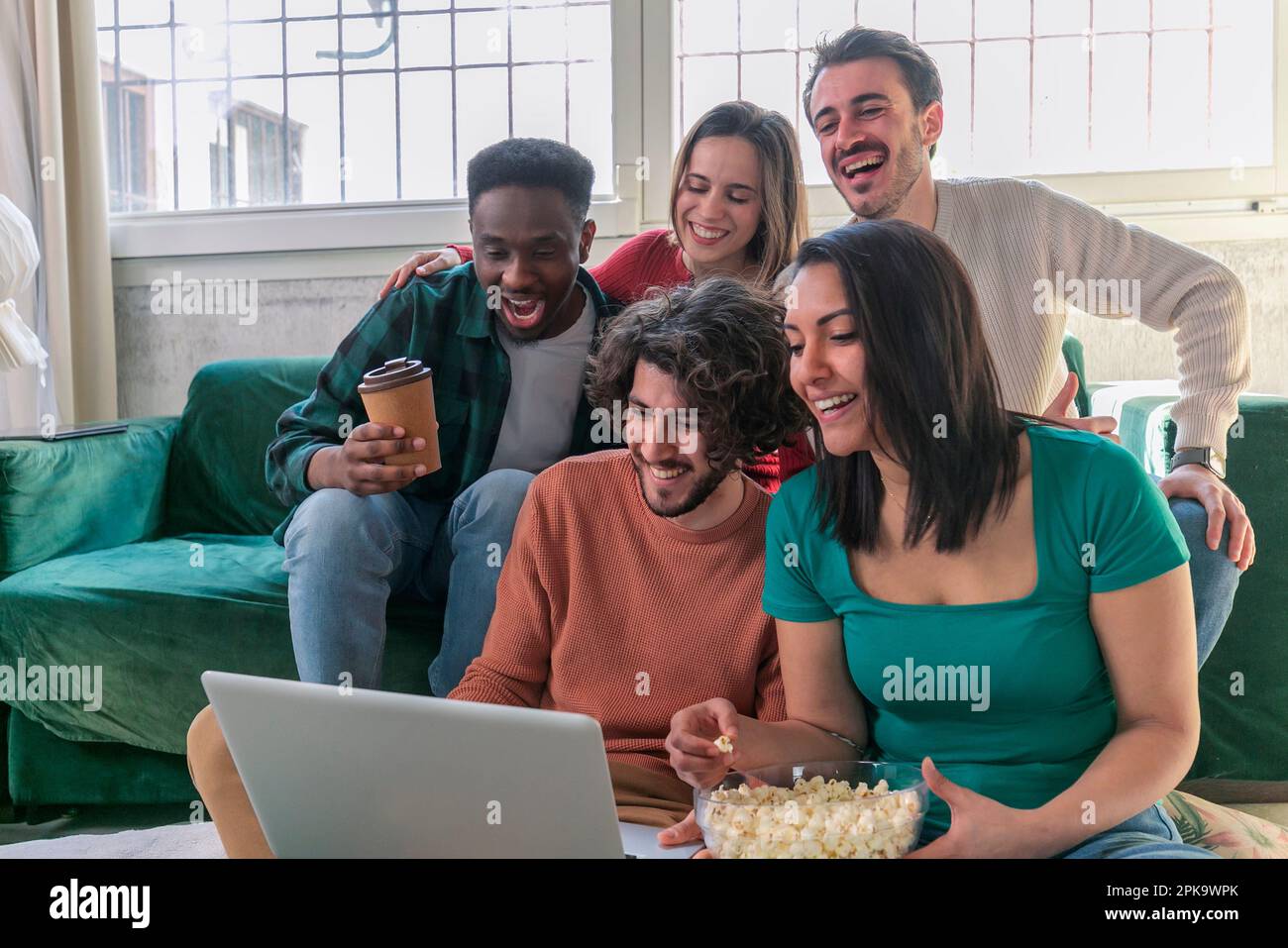 Un gruppo di giovani amici con un computer portatile seduto sul divano al coperto, guardando film. Foto Stock