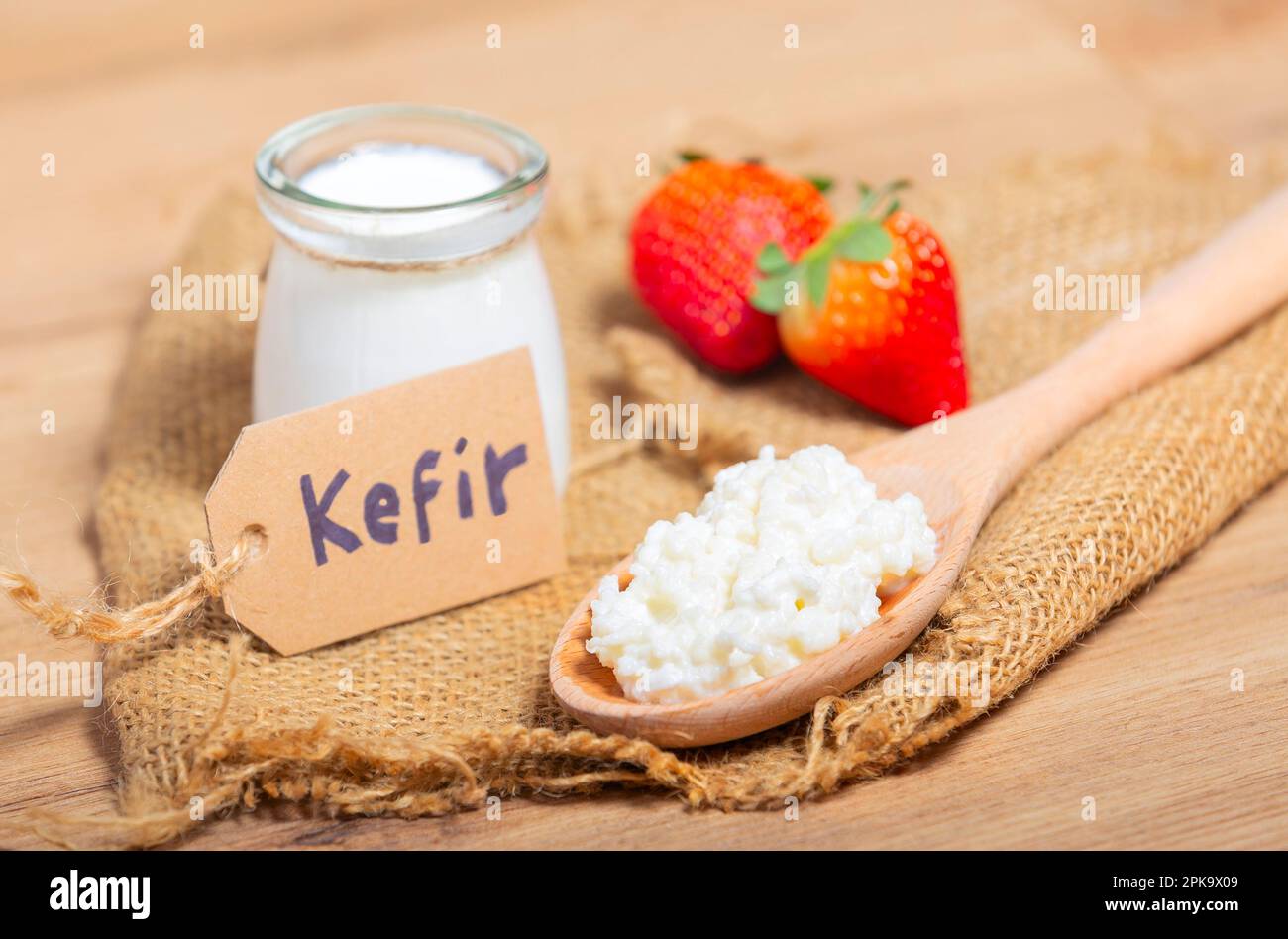 Grani di kefir in cucchiaio di legno davanti a tazze di yogurt di kefir parfaits. Kefir è uno dei migliori alimenti per la salute disponibili fornendo probiotici potenti. Foto Stock