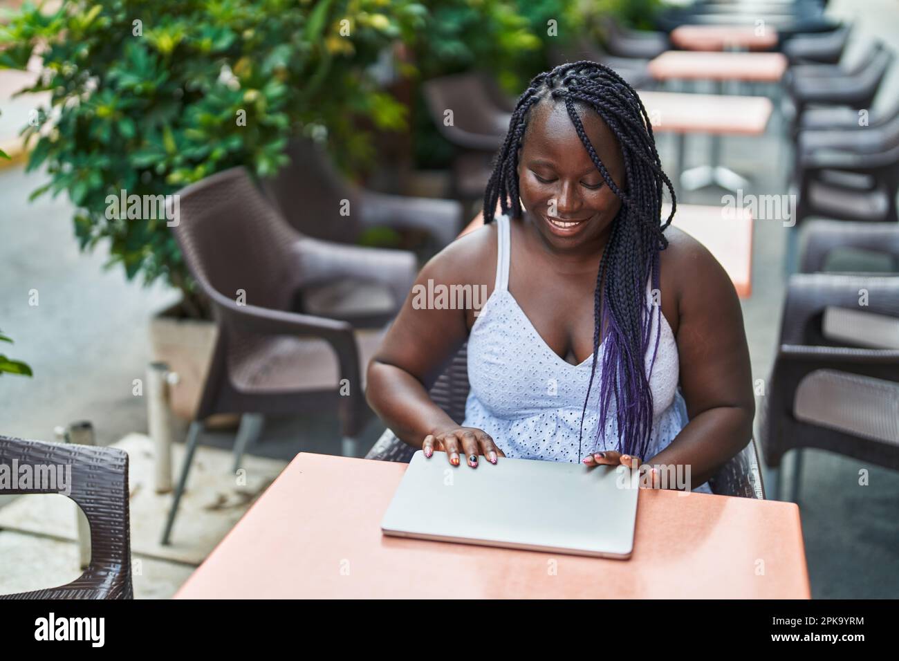 Donna afroamericana che chiude il computer portatile seduto sul tavolo al bar terrazza Foto Stock