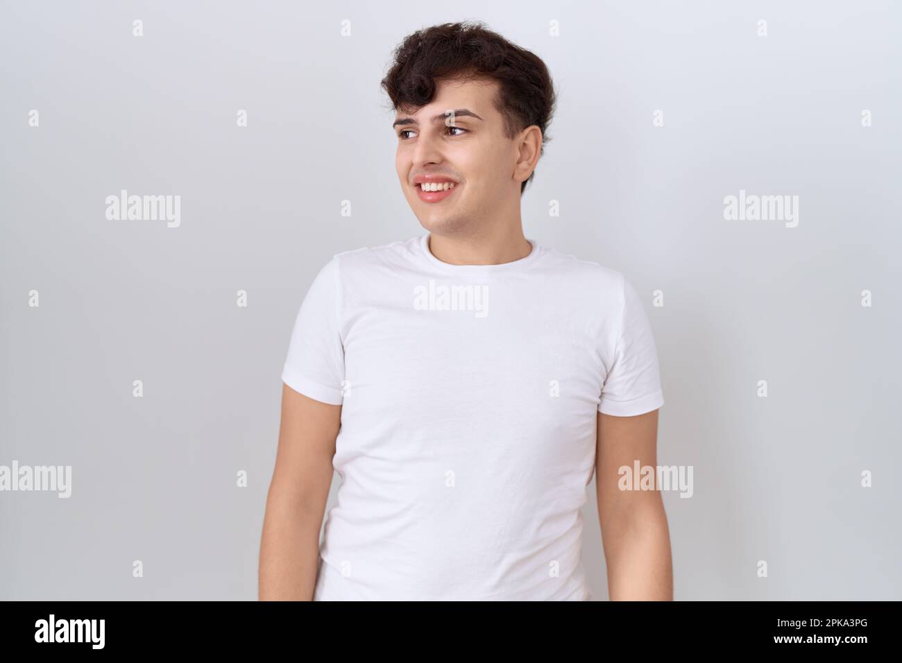 Giovane uomo non binary che indossa casual t shirt bianca guardando da parte con sorriso sul viso, espressione naturale. ridendo fiducioso. Foto Stock