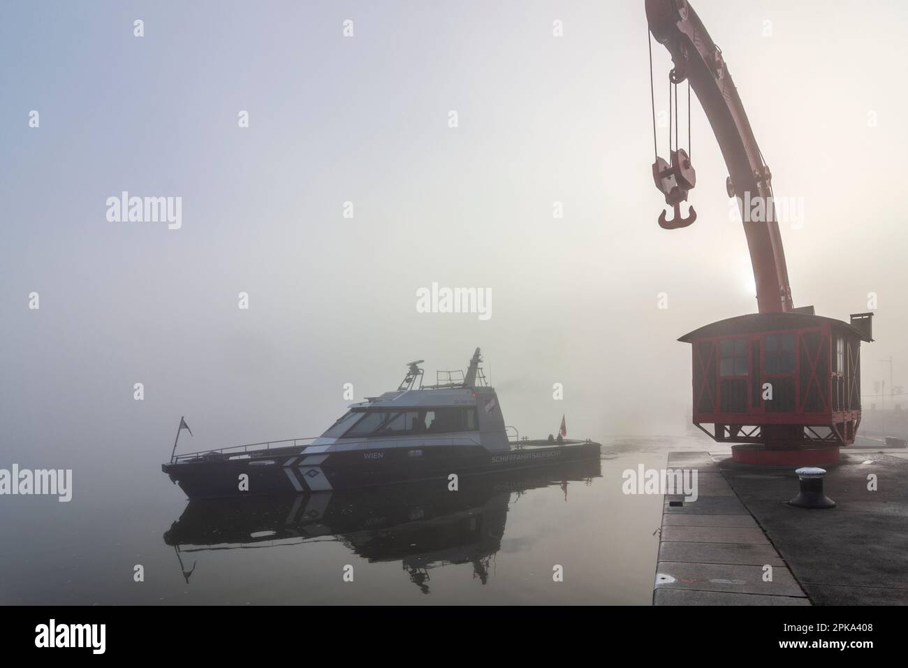 Vienna, nebbia sul fiume Donau (Danubio), vecchia gru portuale, barca di Schifffahrtsaufsicht (supervisione della spedizione) si sposta nel 02. Leopodstadt, Austria Foto Stock