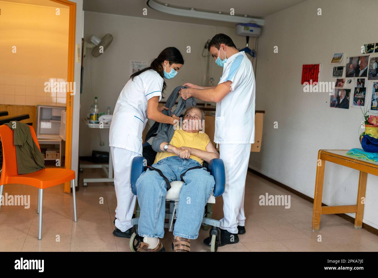Due assistenti infermieri mettono un paziente disabili a letto nella sua stanza presso la casa di cura. Foto Stock