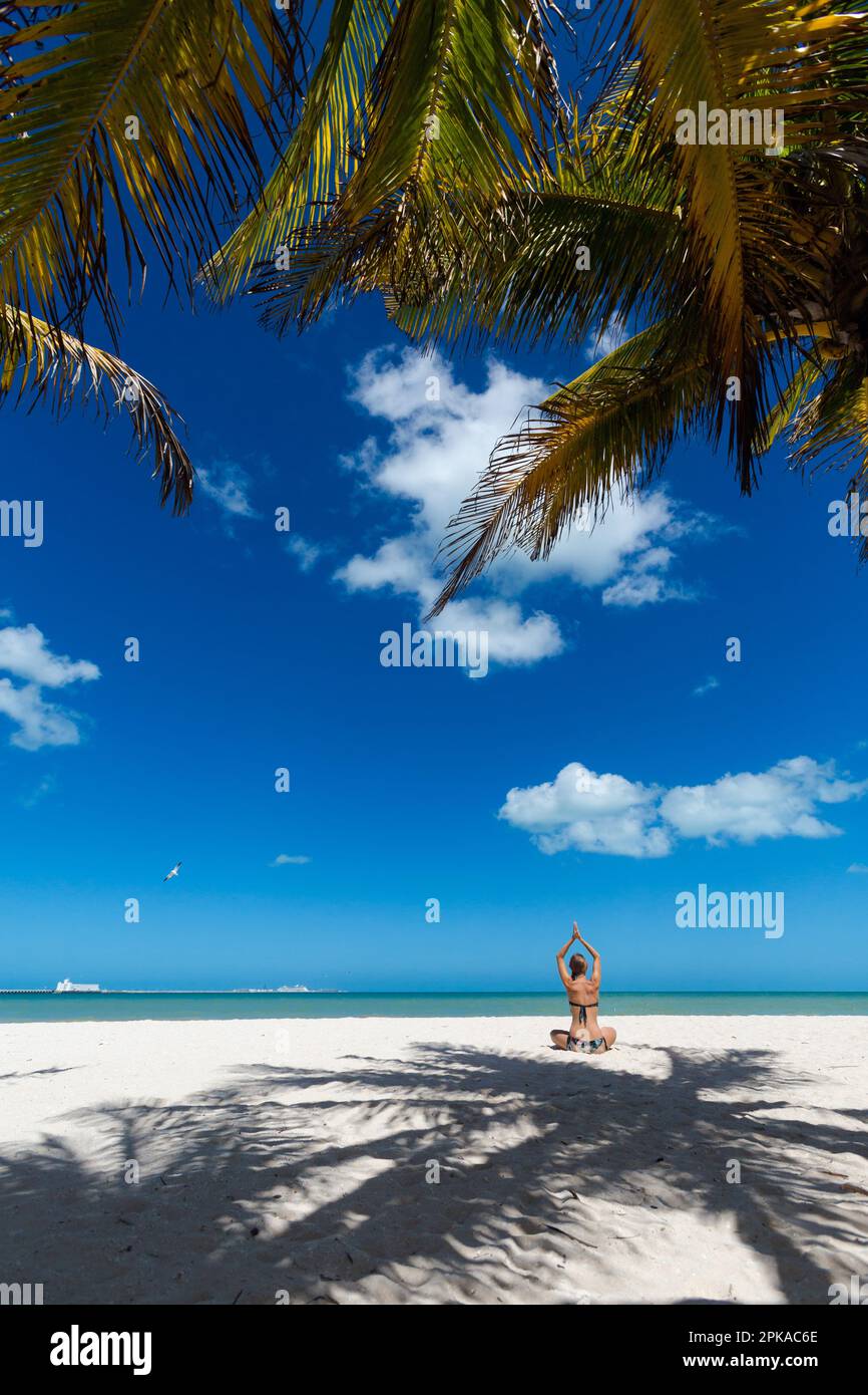 Bella giovane donna meditando su una spiaggia Progero Messico durante il giorno di sole. Spiaggia bianca con palme e cielo blu. Foto Stock