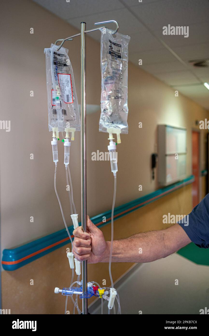Mano del paziente che tiene un'infusione in un corridoio ospedaliero. Foto Stock
