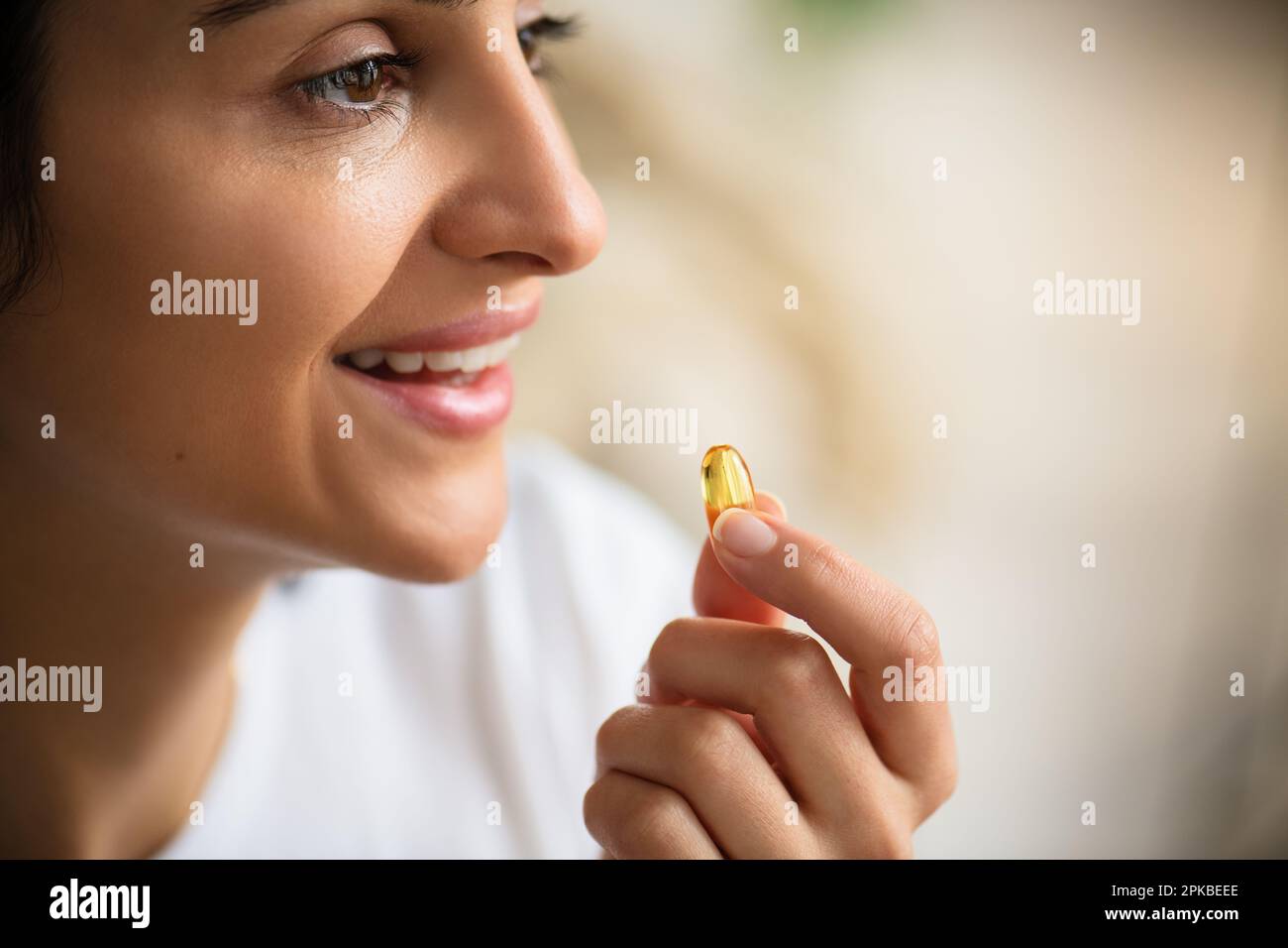 Multirazziale sorridente giovane donna che prende una capsula di olio di pesce Omega-3 a casa con denti bianchi, la donna prende e beve cibo integratori alimentari vitamine Foto Stock