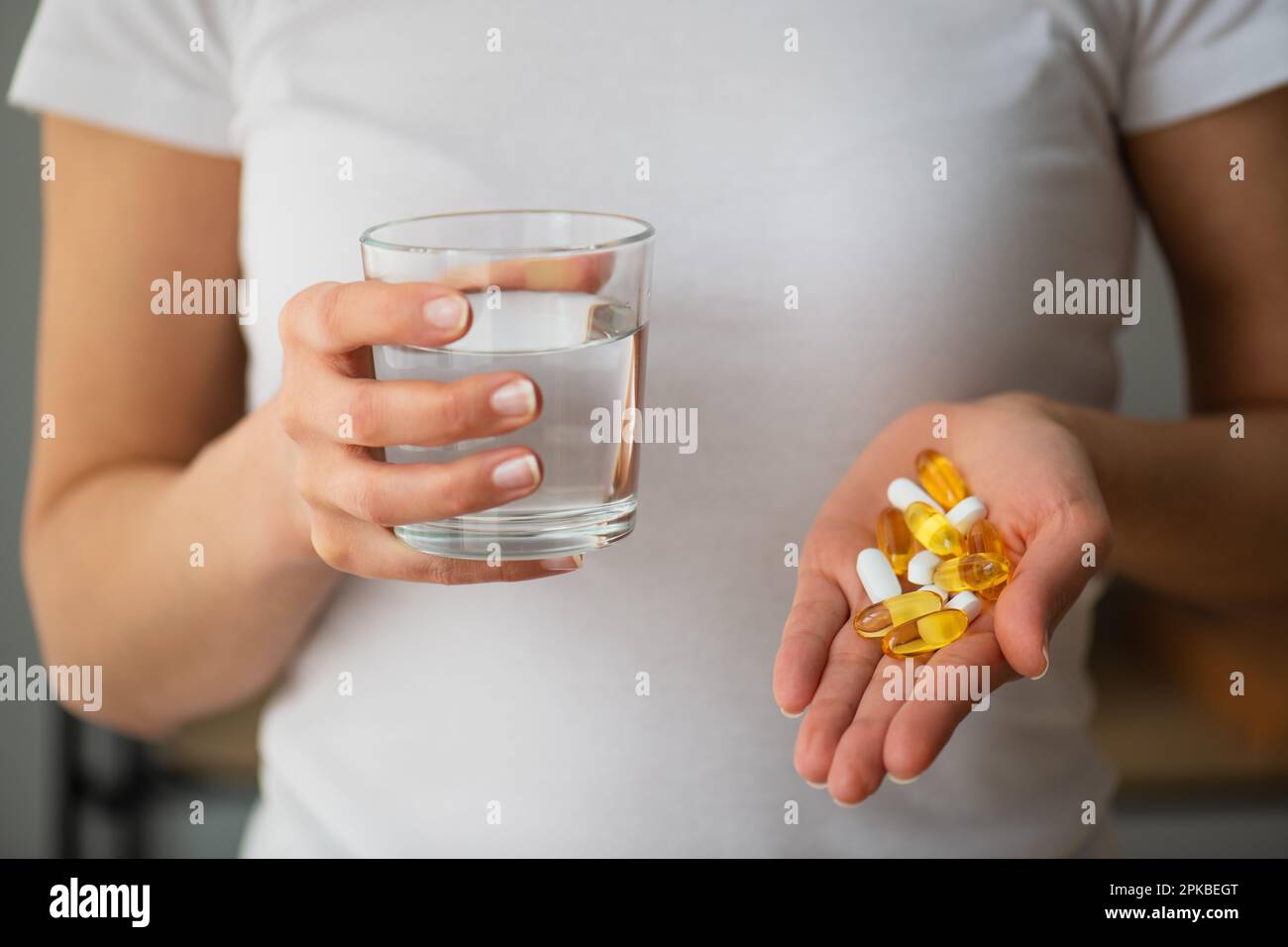 Primo piano le mani femminili in possesso di olio di pesce Omega-3 pillole e un bicchiere d'acqua, in piedi a casa, stile di vita sano un concetto di medicina Foto Stock