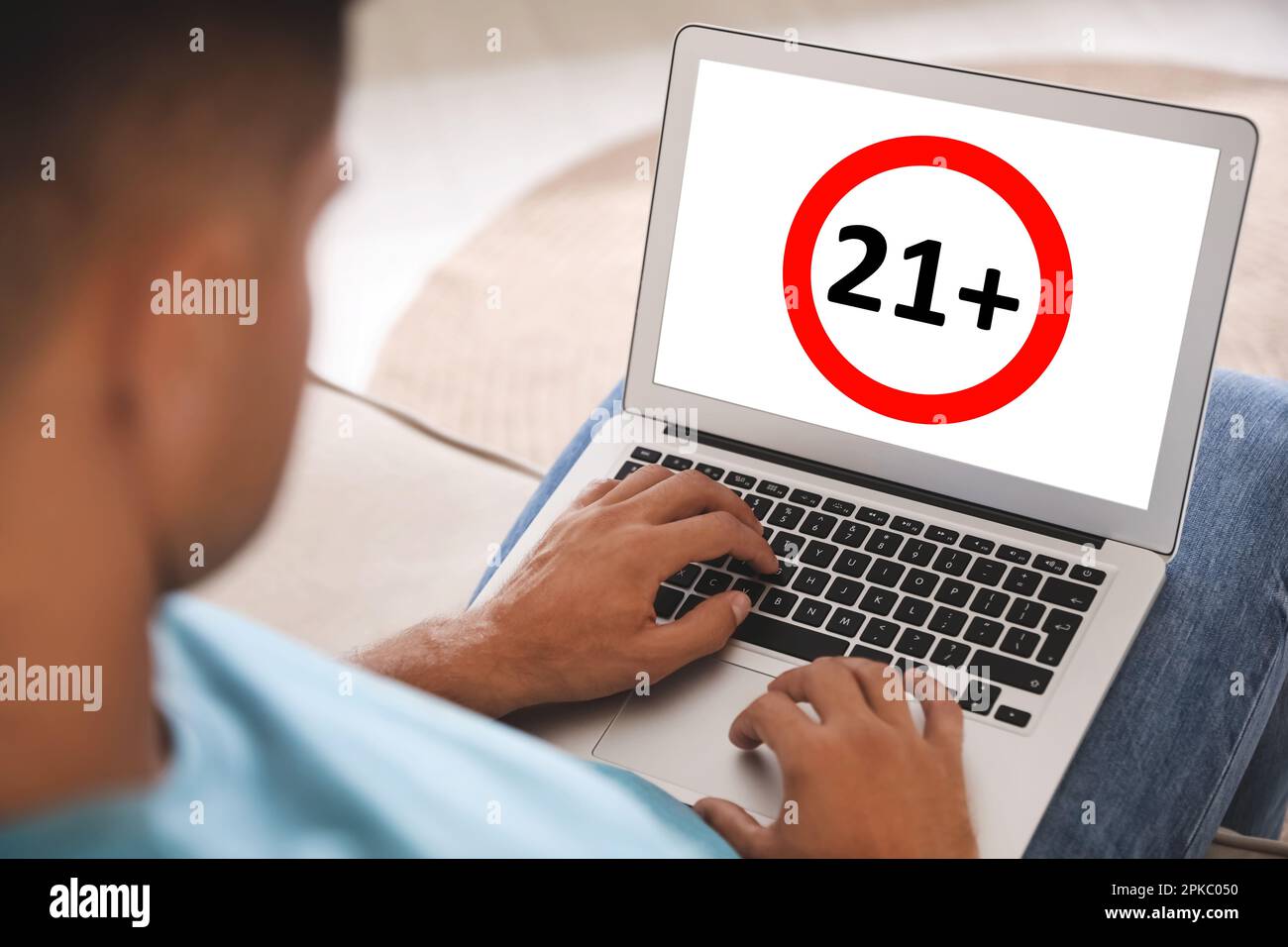 Uomo che utilizza un notebook con limite di età segno 21+ anni in ambienti chiusi, primo piano Foto Stock